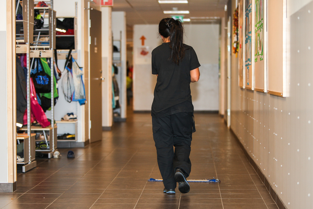 woman custodian sweeping the school hallway floor.